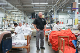 Man standing between working inmates at sewing shop