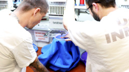 Inmate showing another inmate how to embroider a shirt