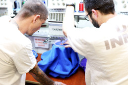 Inmate showing another inmate how to embroider a shirt