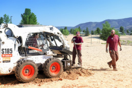 Inmates operating heavy machinery to dig hole to install volleybal post