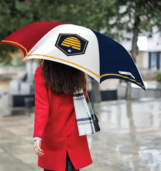 Lady in red coat walking on a rain covered street with an umbrella sporting the new Utah state flag printed